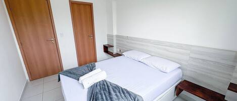 A bedroom with a bed, two wooden doors, a bedside table, and a nightstand.