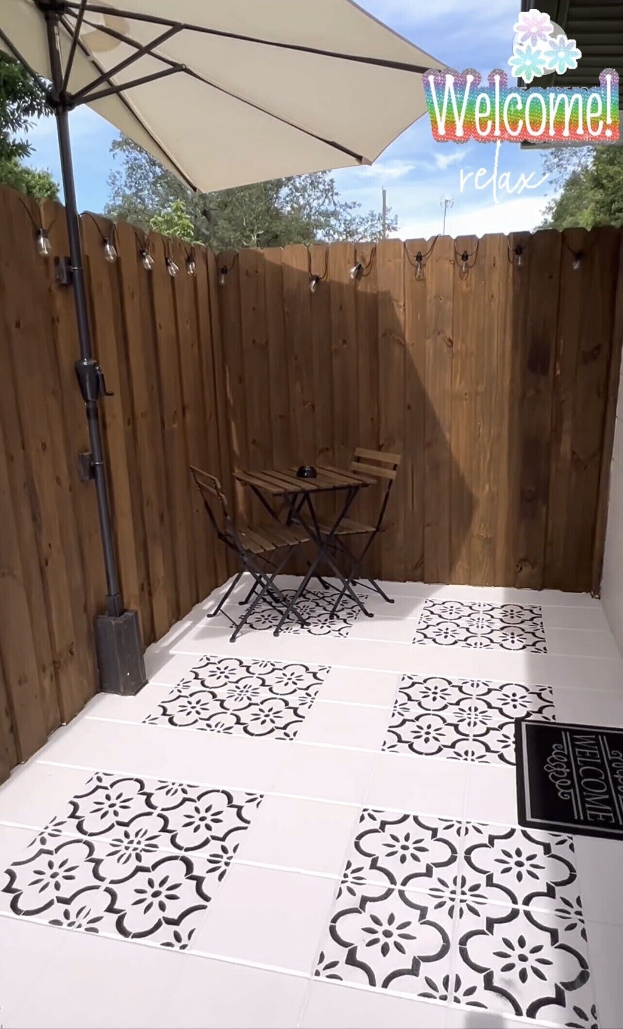 A patio area with a wooden fence, a table with chairs, and patterned floor tiles.