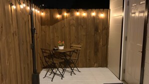 Un patio con cerramiento de madera, una mesa con sillas y una puerta blanca.