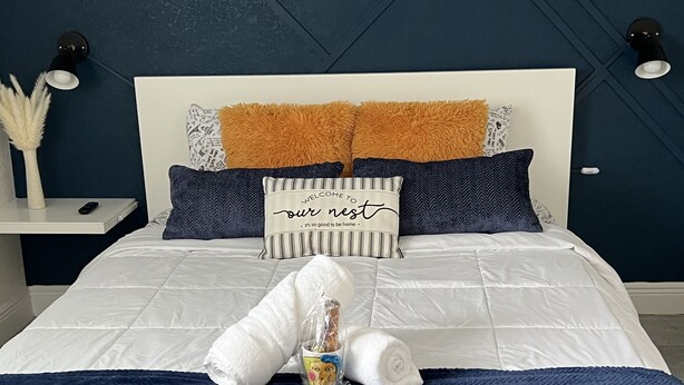 Una cama bien hecha con una colcha blanca, un edredón azul marino y almohadas decorativas.