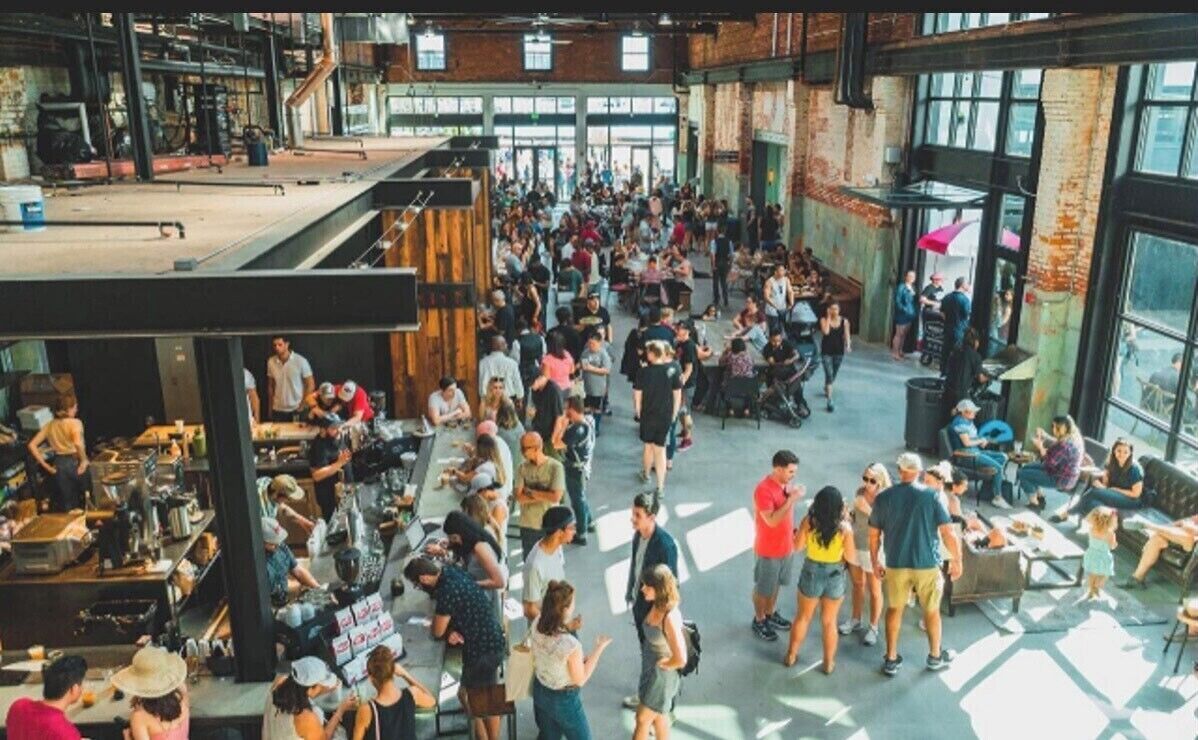 A spacious, open-plan venue with high ceilings and large windows, featuring a central open area surrounded by seating and tables.