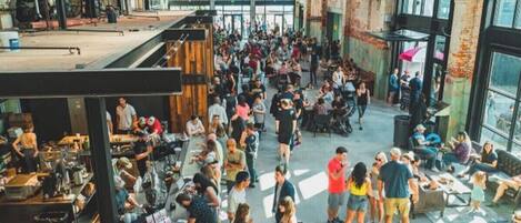 A spacious, open-plan venue with high ceilings and large windows, featuring a central open area surrounded by seating and tables.