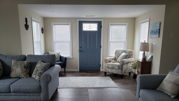 A living room with a grey sofa, a floral armchair, a coffee table with a tray of decorative items, and a door with a window. - Minutes to DE TURF FIELDS.  Quiet beach community.   (Frederica)