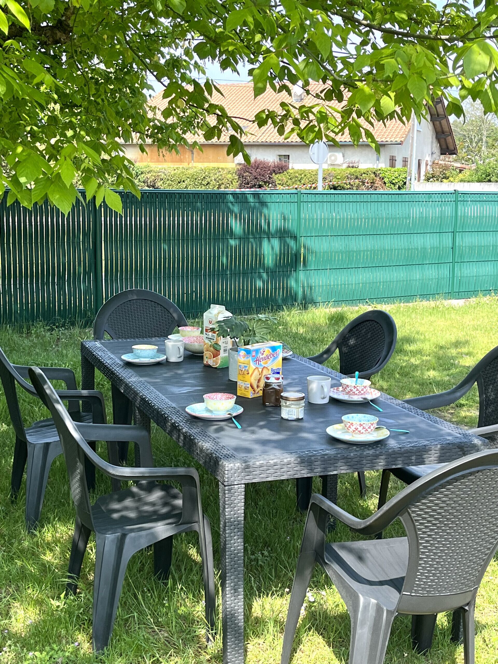 Un espace de restauration en plein air avec une table dressée pour quatre personnes, entourée de chaises, sous un arbre.