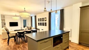 Een moderne keuken met een centraal eiland, een eethoek met stoelen en een aan de muur bevestigde televisie.