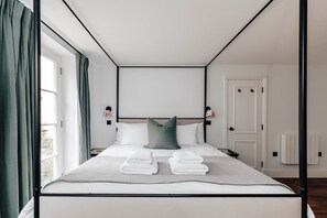 A modern hotel room with a large bed, a view through the window, and a door.