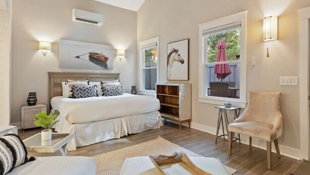 A bedroom with a large bed, bedside tables, a chair, a window with a view, and artwork on the walls. - Minutes to Downtown Charleston, Shem Creek & Beach (Mount Pleasant)