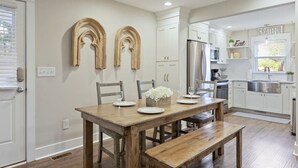 A modern kitchen with white cabinetry, a wooden dining table, and a built-in oven. - Minutes to Downtown Charleston, Shem Creek & Beach (Mount Pleasant)