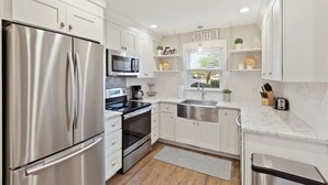 A modern kitchen with stainless steel appliances, white cabinetry, and a window with a view. - Minutes to Downtown Charleston, Shem Creek & Beach (Mount Pleasant)