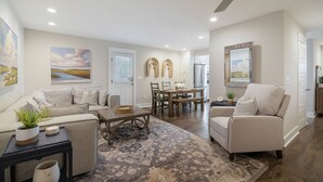 A spacious living room with a sofa, a coffee table, and a dining area with a table and chairs. There is a ceiling fan and recessed lighting. - Minutes to Downtown Charleston, Shem Creek & Beach (Mount Pleasant)