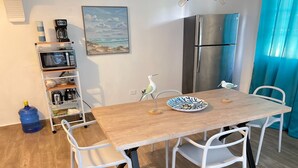 A dining area with a wooden table, white chairs, a blue water dispenser, a coffee machine, a refrigerator, and a shelf with kitchen items. - recently renovated 2 Bedroom Apt, on the 2nd floor with free parking (Los Melones)