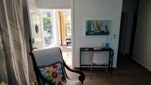 A living room with a white armchair, a small table with books, a painting of sailboats on the wall, and a view of the outside balcony. - recently renovated 2 Bedroom Apt, on the 2nd floor with free parking (Los Melones)