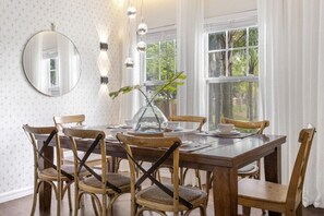 Une salle à manger avec une table en bois, six chaises, un miroir rond et un vase avec une plante.