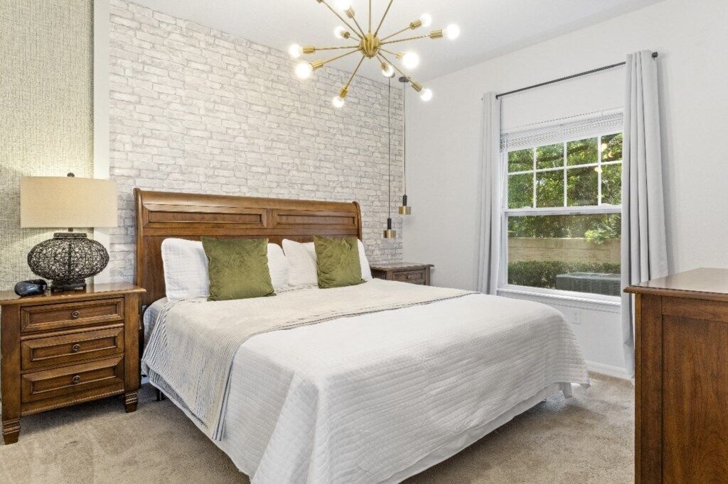 Een slaapkamer met een bakstenen muur, een houten bed, een nachtkastje, een lamp en een raam met gordijnen.