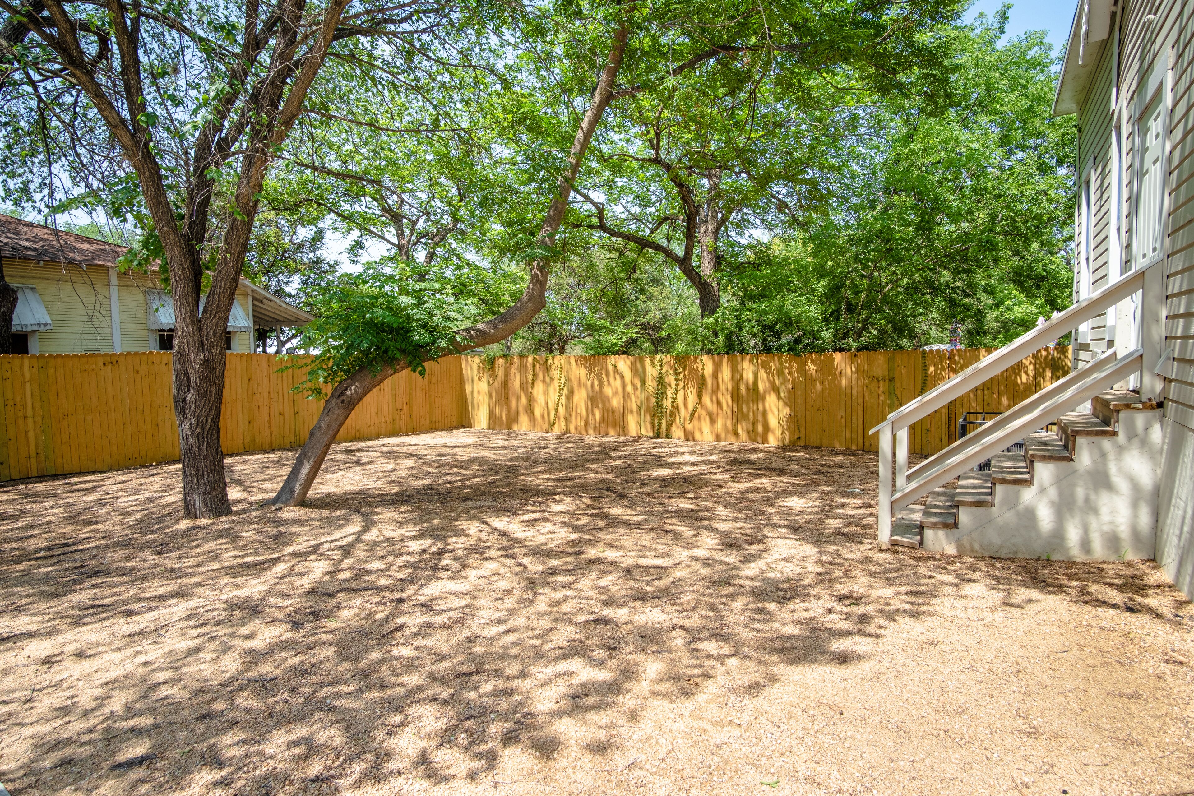 A backyard with a wooden fence, a tree, and a staircase leading to a house.
