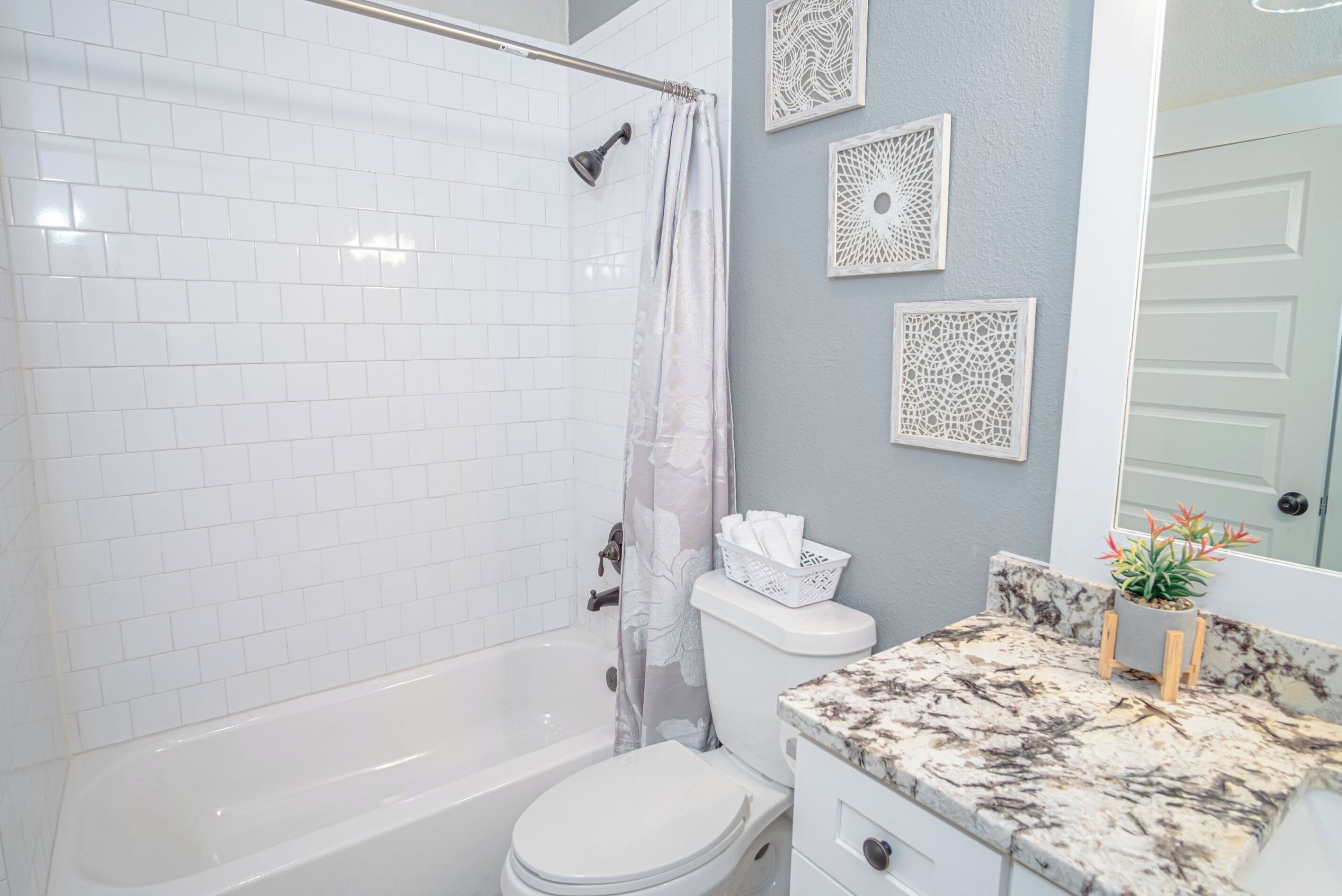 Une salle de bain avec une baignoire blanche, des toilettes et un rideau de douche. Des éléments décoratifs ornent le mur au-dessus du lavabo.