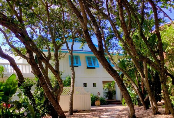 A white building with blue shutters, surrounded by trees and greenery.