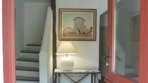 En trappa som leder upp till en liten plattform med ett bord och en lampa, en inramad tavla på väggen och en röd dörr.