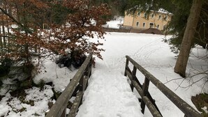 Een houten brug die naar een besneeuwde omgeving leidt, met een gebouw op de achtergrond.