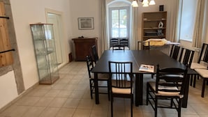 Een eetgedeelte met een lange tafel, stoelen, een kroonluchter en een raam met gordijnen.