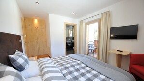A hotel room with a large bed, a TV, a red chair, and a wooden wardrobe. - Apartments Leni 109A (Castelrotto)