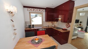 A compact kitchen with a dining table, red cabinets, and a window providing natural light. - Apartments Leni 109A (Castelrotto)