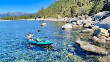A clear lake with a kayak, surrounded by rocks and trees.