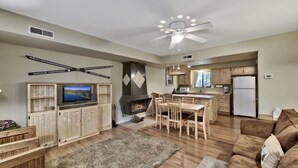 A spacious living area with a fireplace, wooden furniture, a television, and a kitchen with a refrigerator.