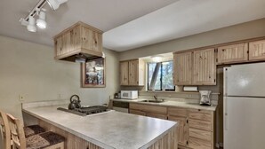 A kitchen with wooden cabinets, a central island, a microwave, a refrigerator, and a window with a view of trees.