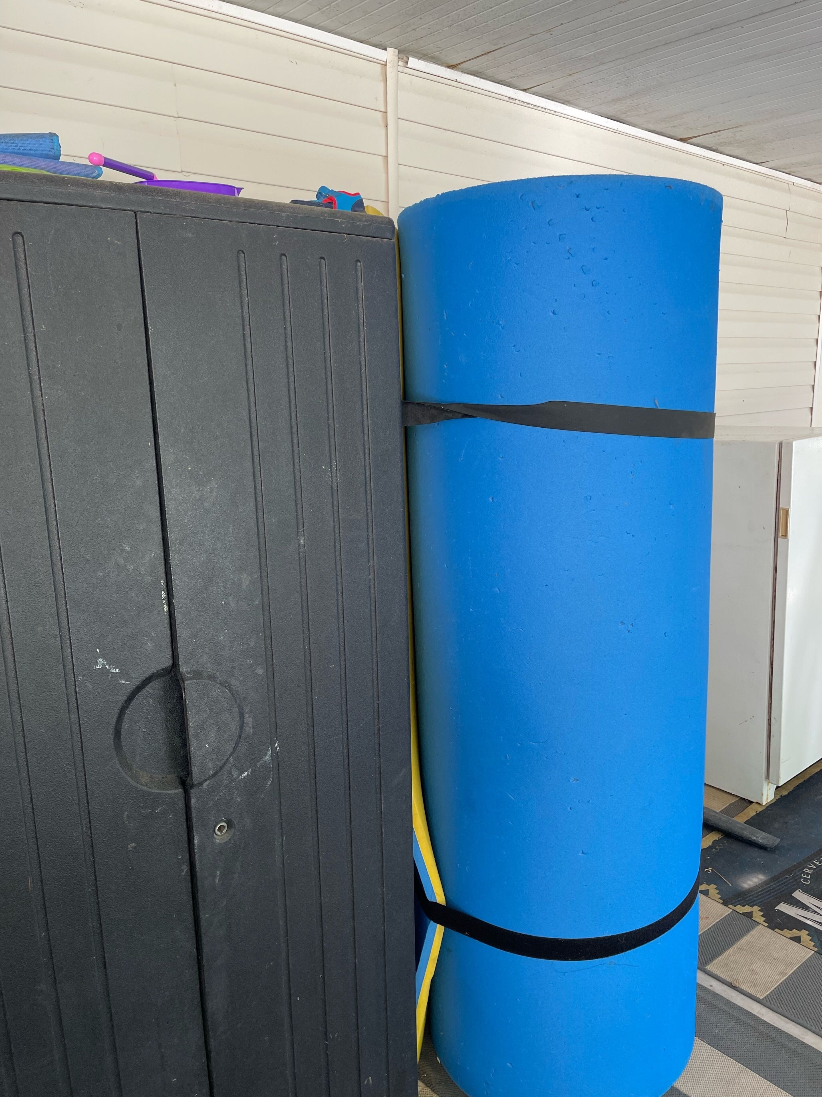 A blue cylindrical object with black bands, a black cabinet, and a white wall with horizontal lines.