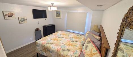 A bedroom with a bed, a television, a window with blinds, and a ceiling fan.