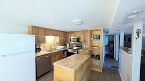 Une cuisine compacte dotée de meubles en bois, d’appareils électroménagers en acier inoxydable et d’un îlot central en bois.