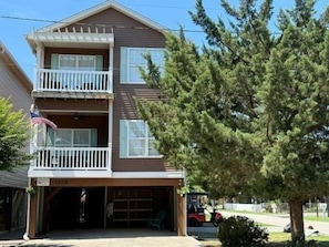 A two-story residential building with a balcony on the upper floor, a garage, and a tree in front.