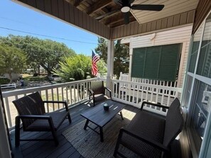 A covered porch with outdoor furniture, a flag, and a window with shutters.