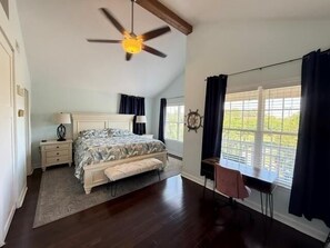 A bedroom with a bed, bedside tables, a desk, a chair, a ceiling fan, and a window with curtains.