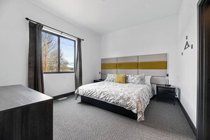 A bedroom with a bed, bedside tables, a desk, a window with curtains, and a view of trees.