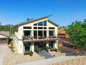 Un bâtiment moderne à deux étages, doté de grandes fenêtres, d’un balcon avec des chaises rouges et d’une entrée pavée de pierres.