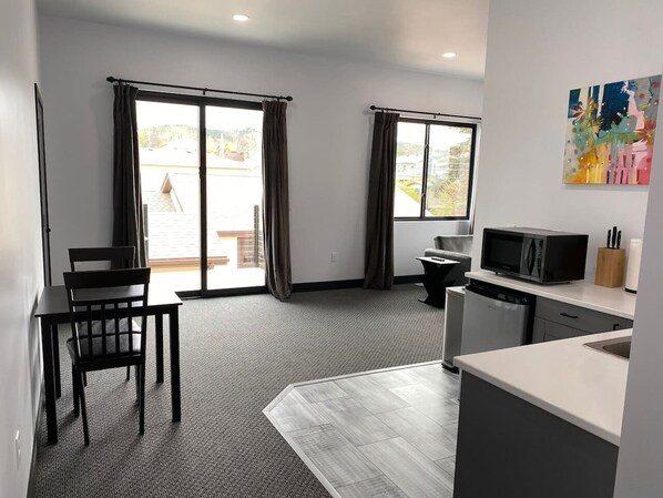 Une chambre moderne équip ée d’une table à manger, de chaises, d’un coin cuisine avec un four à micro-ondes et d’une grande fenêtre avec des rideaux.
