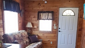 L’intérieur d’un chalet accueillant, avec un plancher en bois, un canapé, une table à manger, un ventilateur de plafond et une porte dotée d’une fenêtre.
