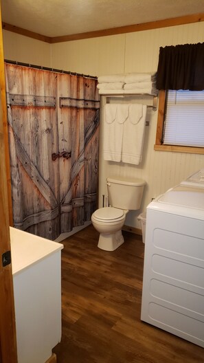 Une salle de bain avec une porte en bois rustique, des toilettes, un lavabo et une fenêtre avec un rideau.