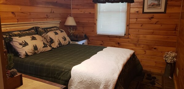 Une chambre confortable avec un lit, une table de chevet, une lampe et une fenêtre avec des stores.