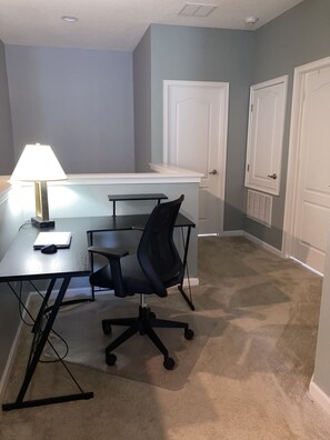 Un petit bureau comprenant un bureau, une chaise, une lampe et deux portes.