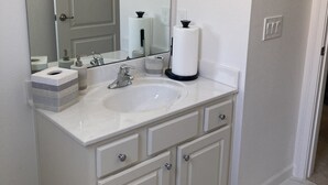 Un baño con lavamanos blanco, tocador doble y un espejo grande. Se observan dos dispensadores de toallas empotrados en la pared y un porta papel higiénico.