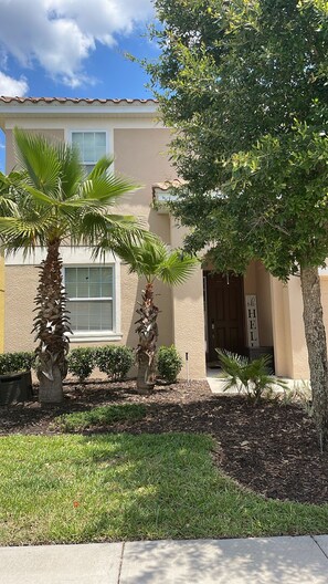 Stroll through the beautifully landscaped yard, featuring two palm trees and a charming entrance.
