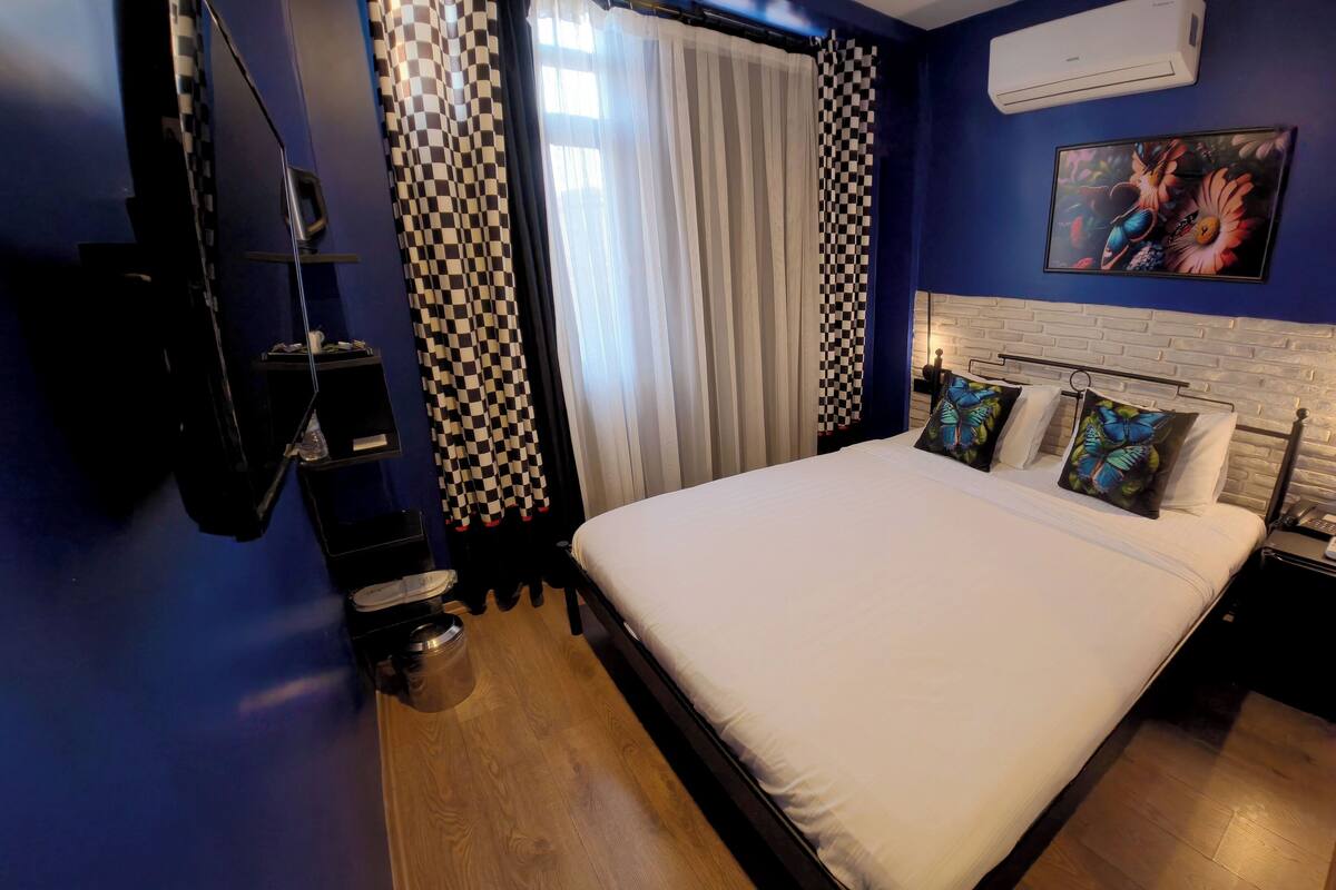 A hotel room with a bed, a nightstand, a wall-mounted air conditioner, and a painting.