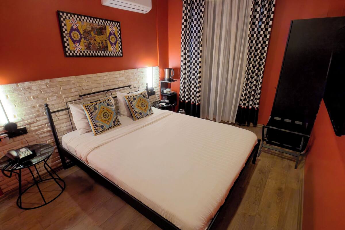 A hotel room with a large bed, a small table with a phone, a wall-mounted TV, and a checkered curtain.