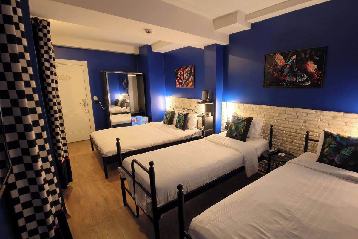 A hotel room with two single beds, a mirror, a small table, and a wall-mounted TV.