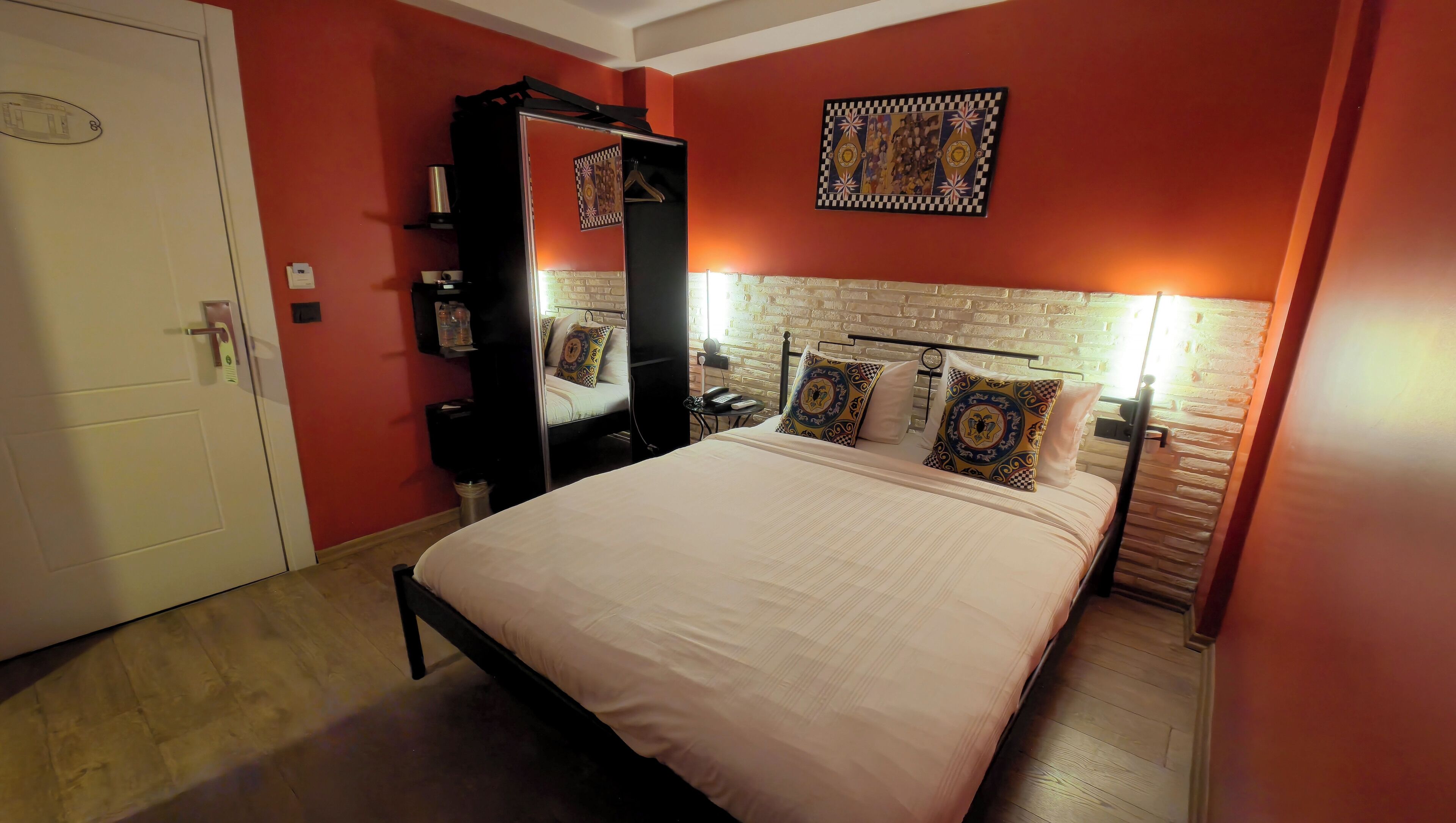 A bedroom with a bed, a wardrobe, a mirror, a bedside table, and a wall-mounted artwork.