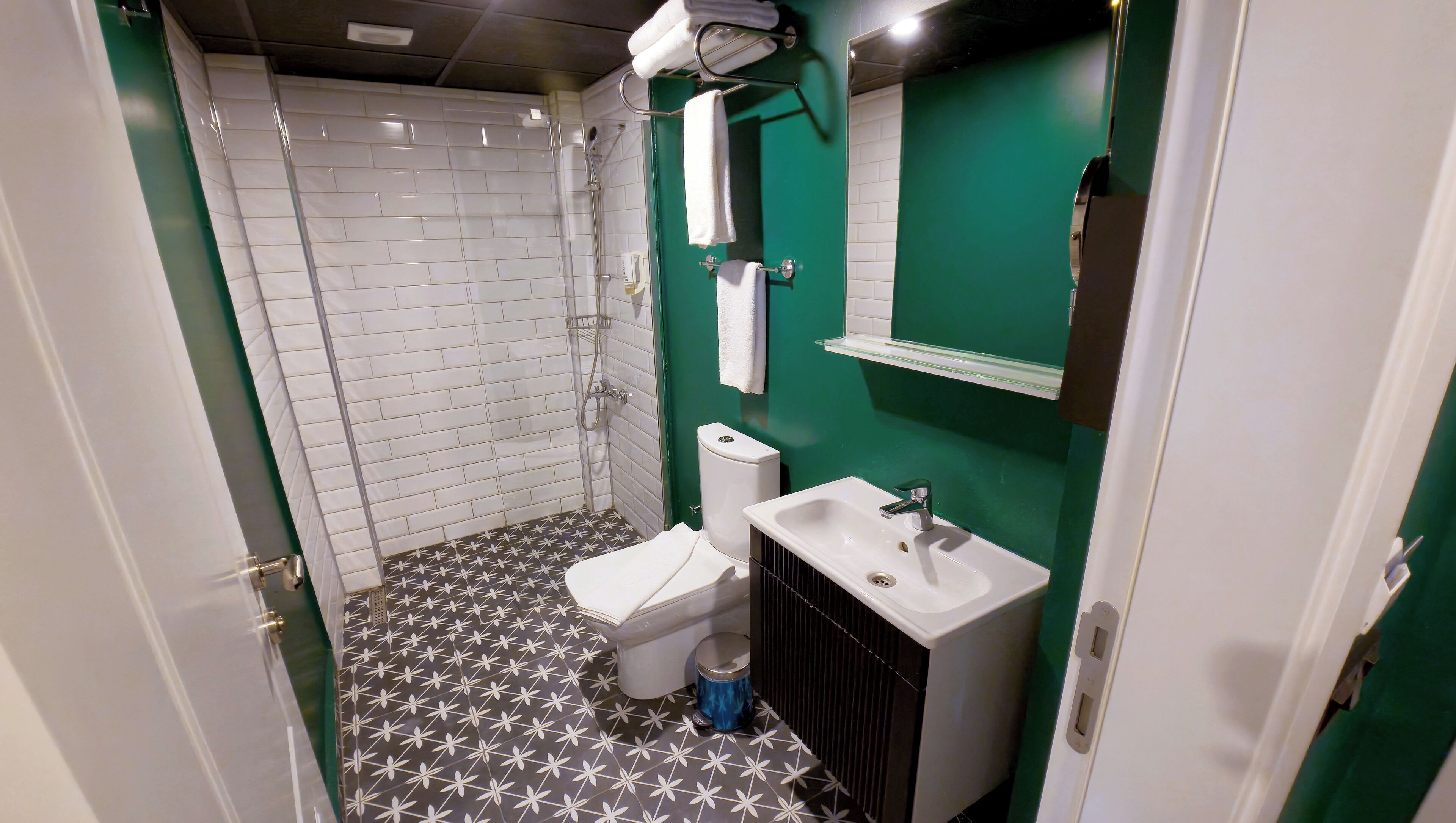 A bathroom with a shower, toilet, sink, and a green wall.