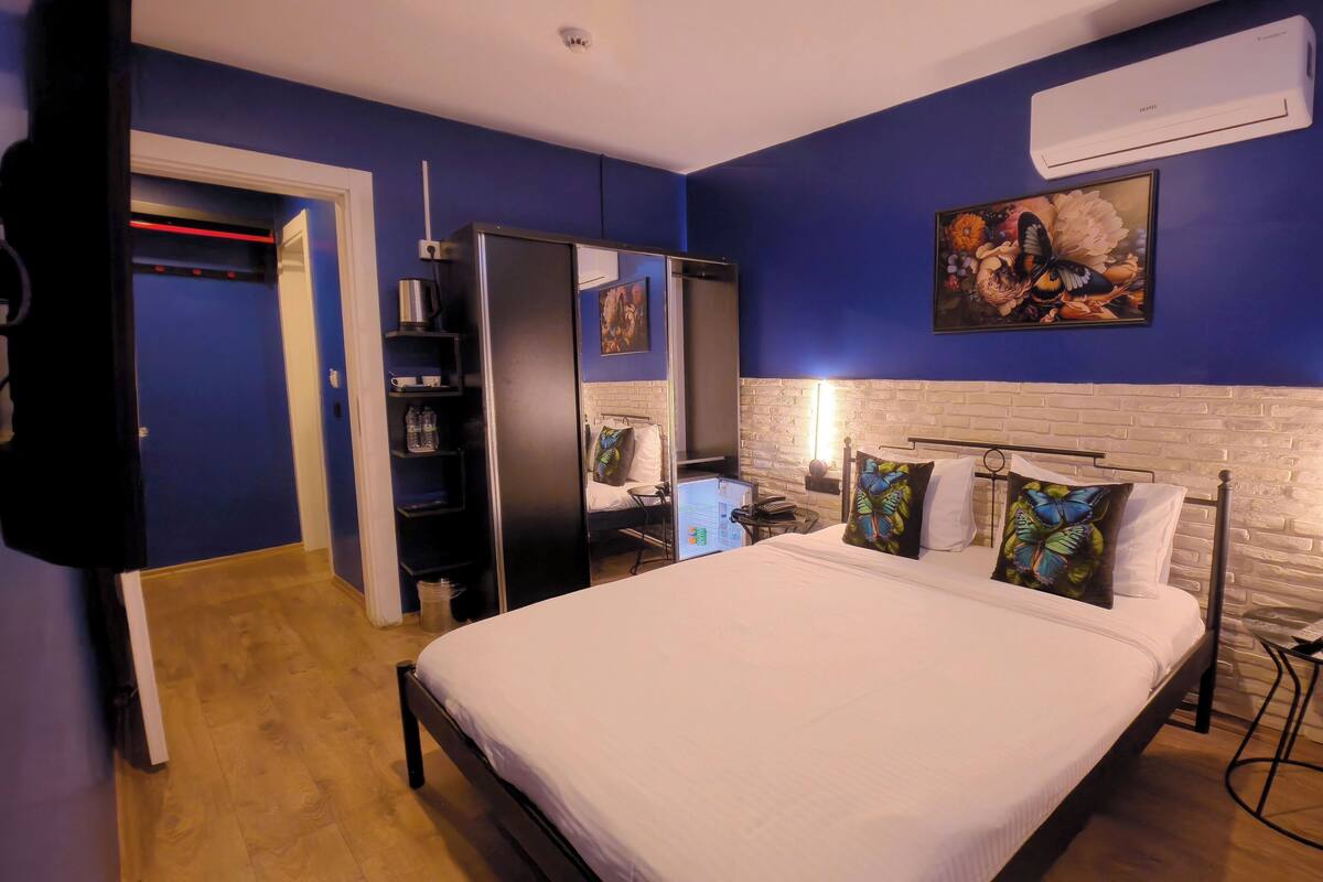 A bedroom with a bed, a wardrobe, a mirror, a desk with a chair, and a wall-mounted air conditioner.